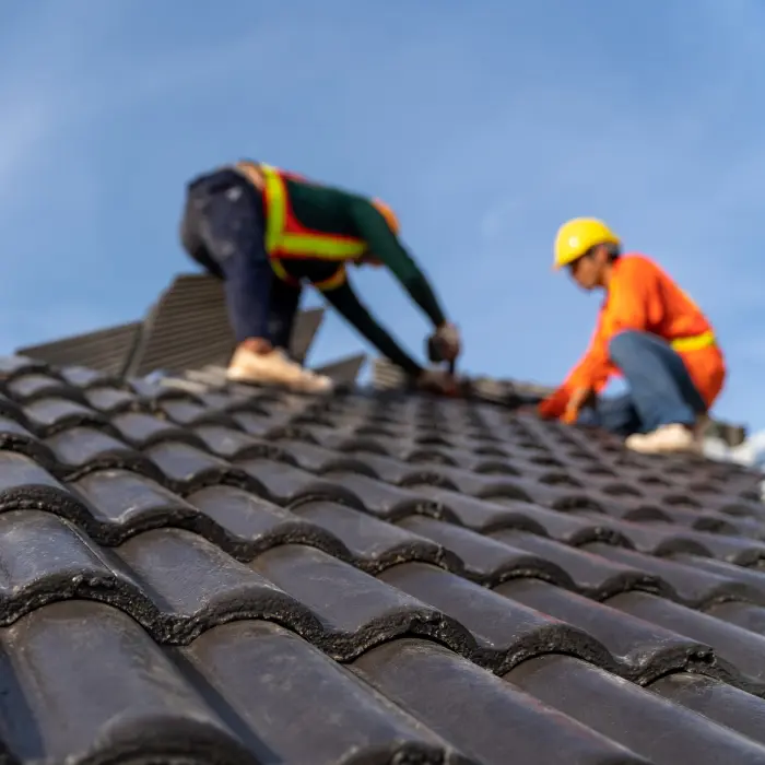 2 roofers working on the working at height to install the Concrete Roof Tiles on the new roof of new modern building construction. Selective focus of Concrete Roof Tiles