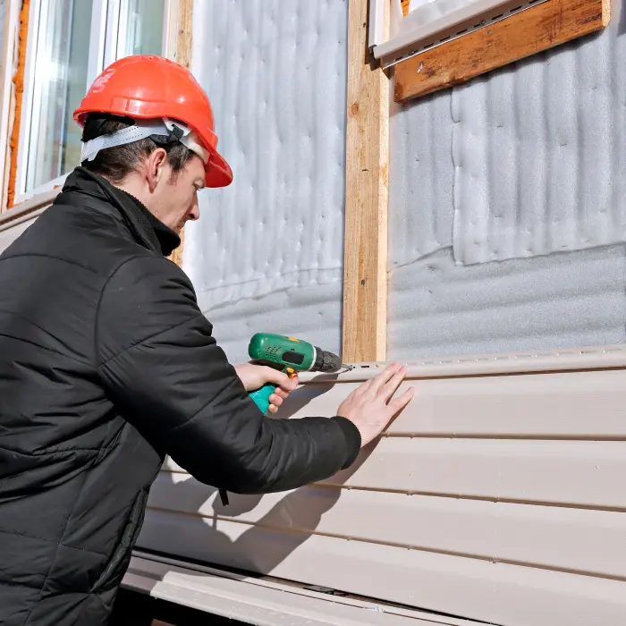 A worker installs panels beige siding on the facade of the house